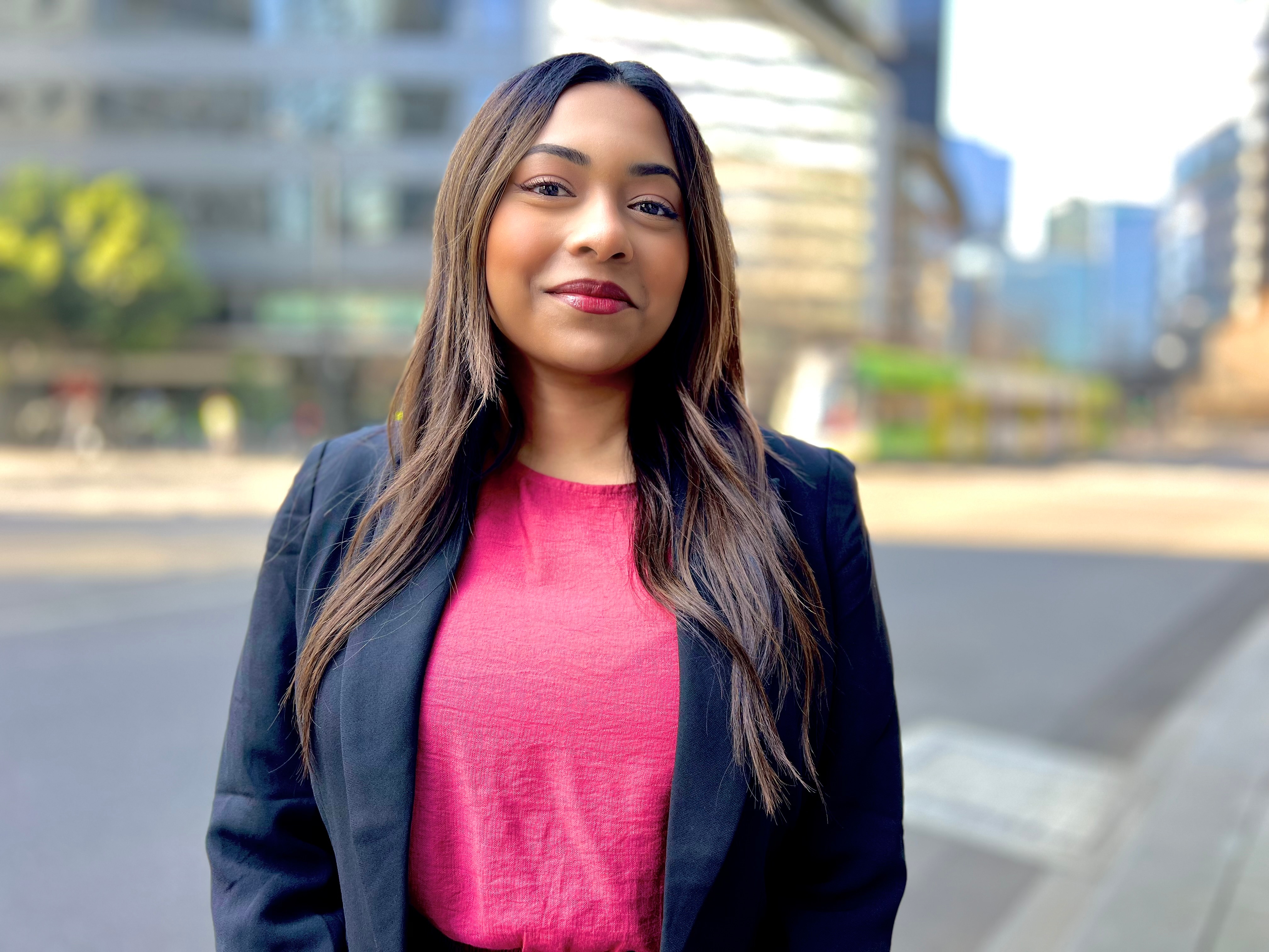A woman in pink shirt standing in city street. 