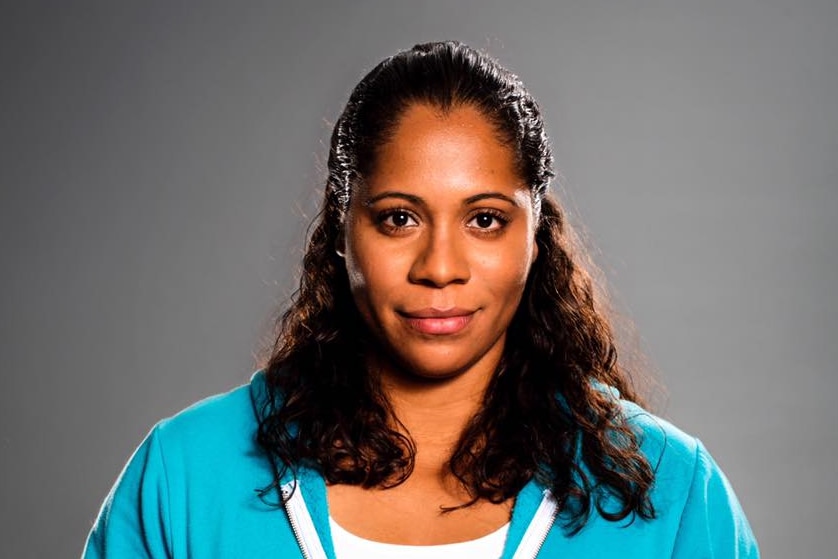 Shareena Clanton smiles, wearing a blue tracksuit standing against a grey backdrop.