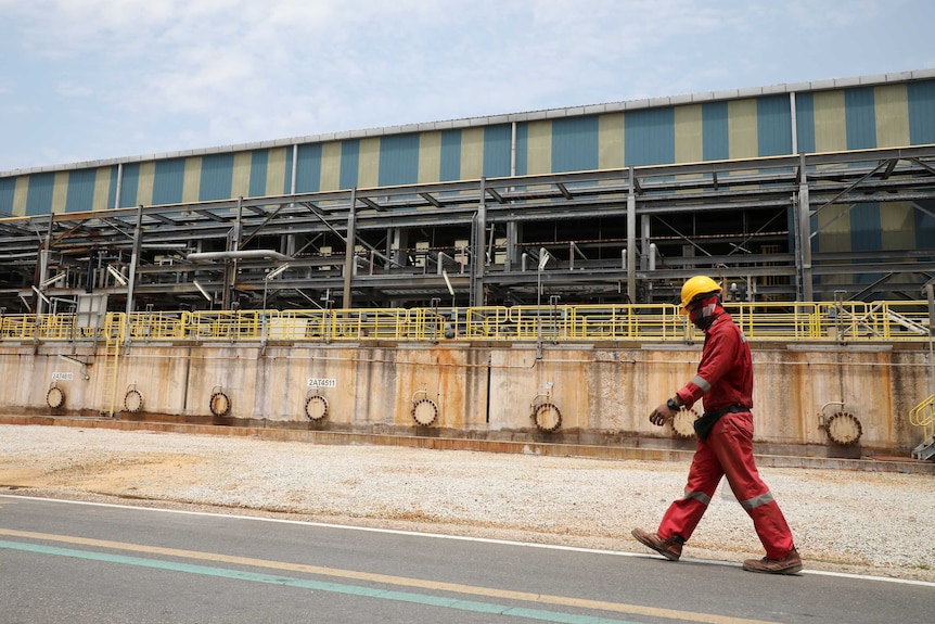A man in hazard gear walks past an industrial building