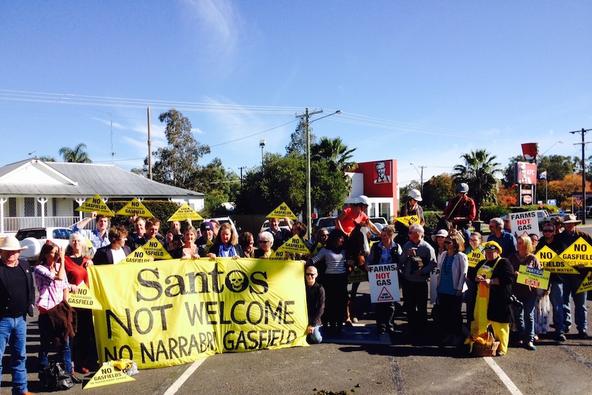 A group of people hold yellow "no gasfields" signs and stand behind a yellow banner.