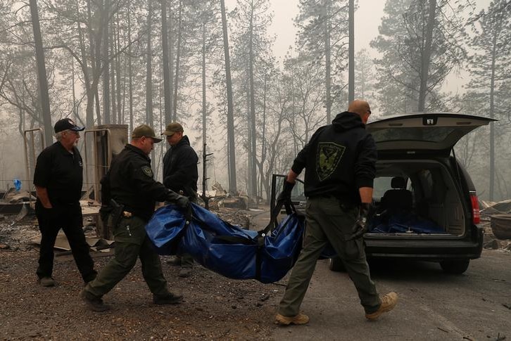 Four Yuba and Butte County Sherriff deputies carry a body bag to a car in the wake of wildfires in Paradise, California