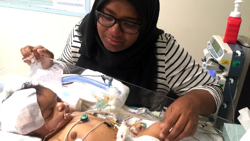 Shizleen Aishath looks at her baby in a hospital bed.