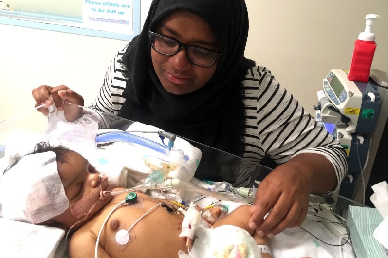 Shizleen Aishath looks at her baby in a hospital bed.