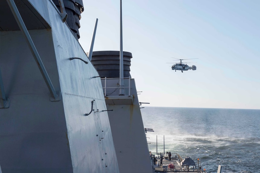 A Russian helicopter flies over a US destroyer