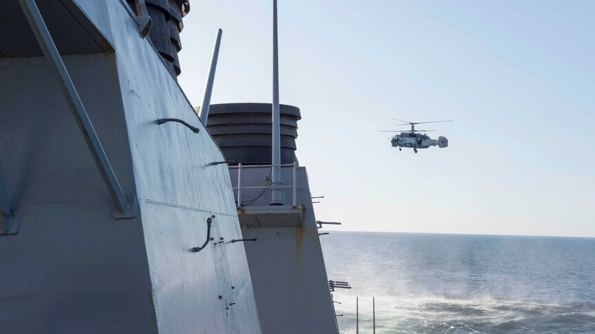 A Russian helicopter flies over a US destroyer