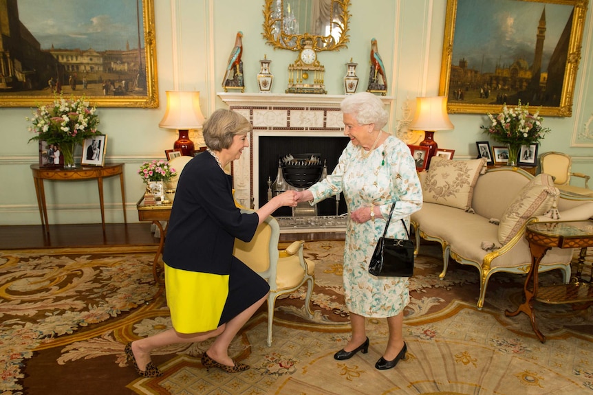 Theresa May kneels as she greets Britain's Queen Elizabeth II.