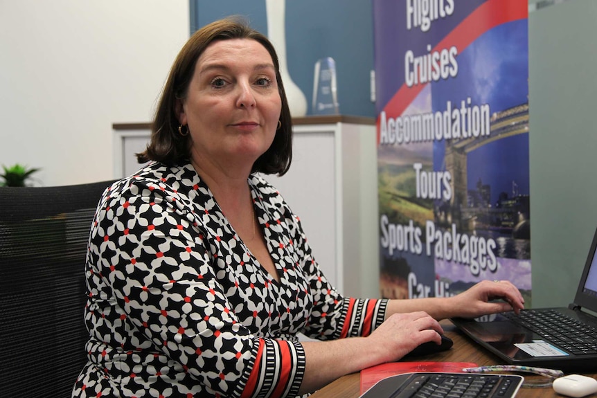 Travel agent Jennie Bardsley sits at her desk in an office wearing a black, white and red top and posing for a photo.