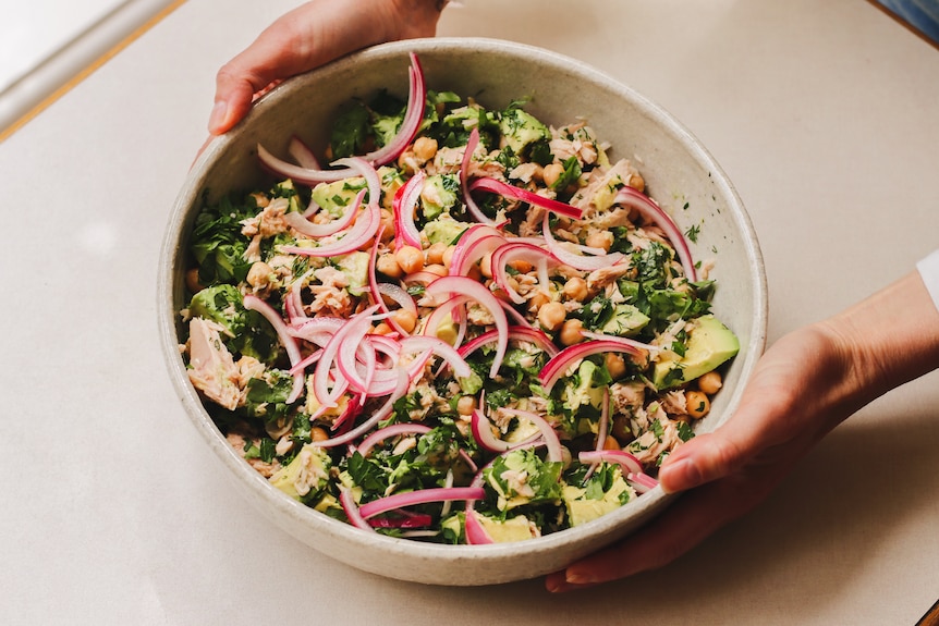 A large bowl of tuna, chickpea and avocado salad on a table. It's topped with pickled red onion, a quick family dinner.