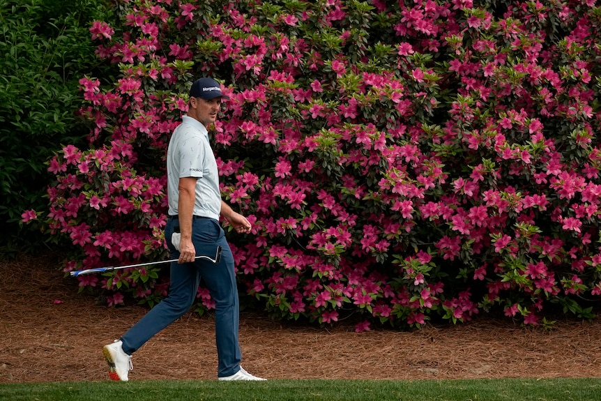 A golfer carries a club as he walks past colourful flowers on the way to the green at Augusta.