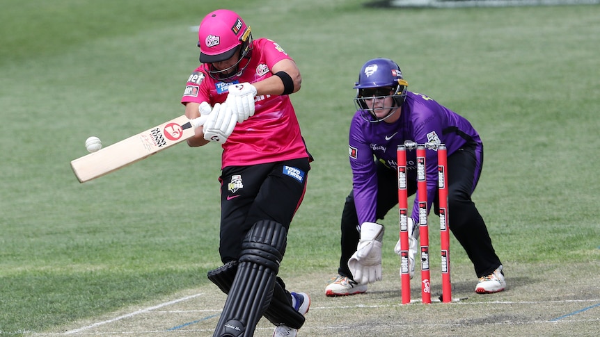 A WBBL batter with her head down swings through the ball as the wicketkeeper watches from behind the stumps.