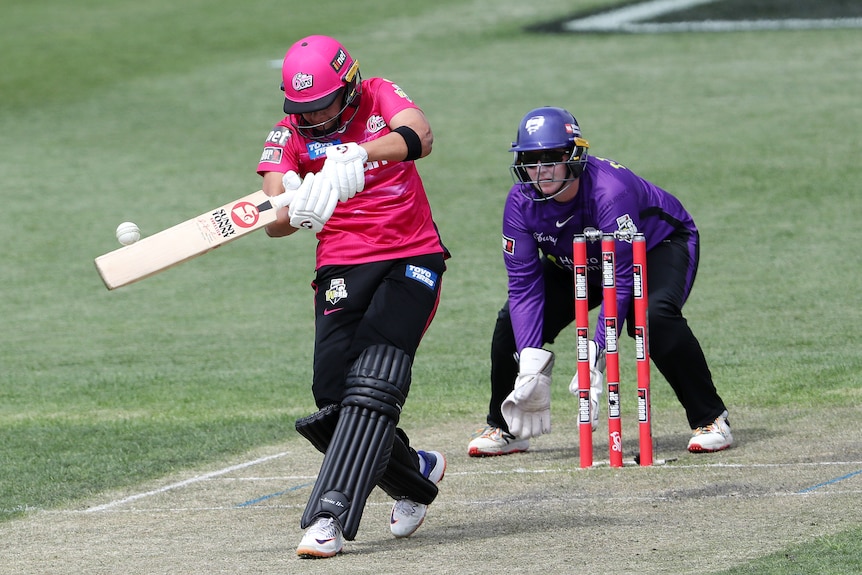 A WBBL batter with her head down swings through the ball as the wicketkeeper watches from behind the stumps.