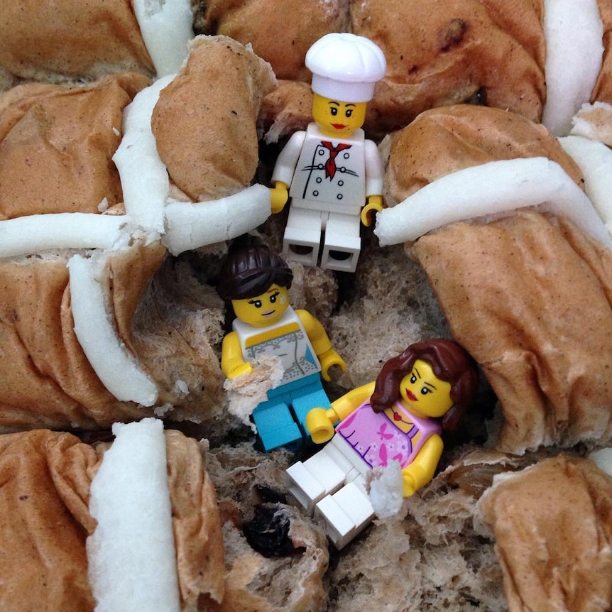 Three lego figurines lying in a pack of hot cross buns.