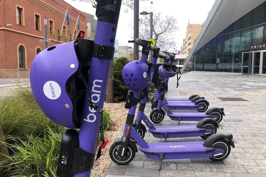 Close-up of a purple Beam e-scooter and helmet with others behind on a street