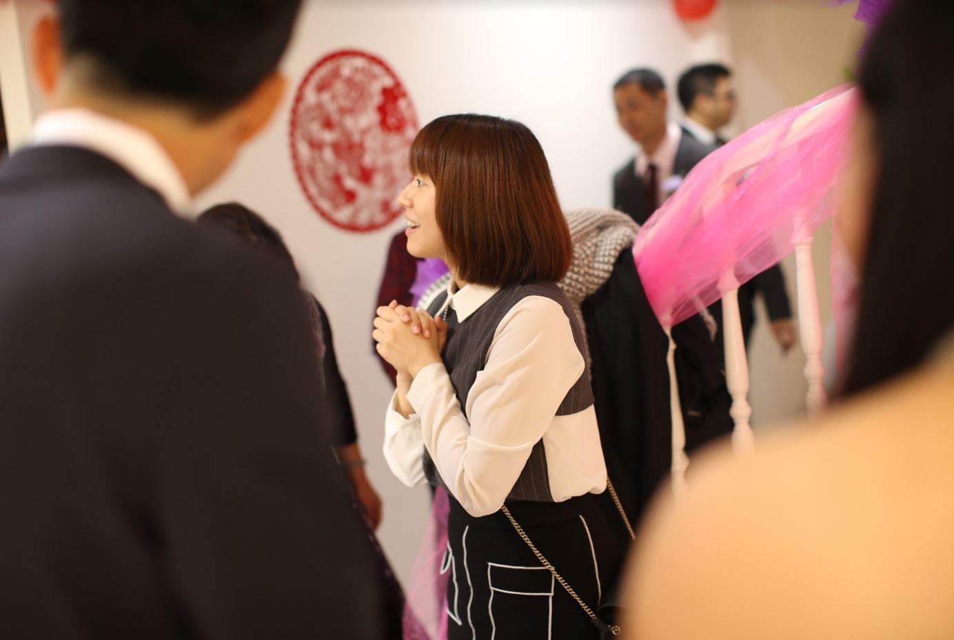 Woman standing centre of frame with her hands clasped.