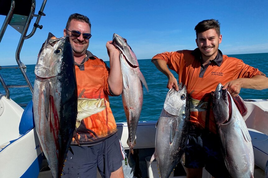Two men on a boat hold up their fish catch.