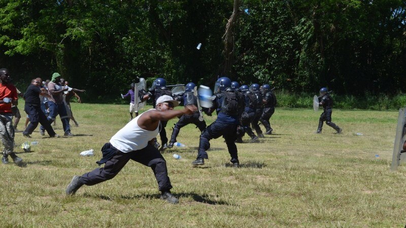 Police armed with shields push back a mock angry mob during a simulation.