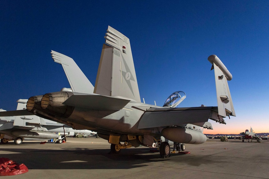 A military plane sits on a tarmac against an evening sky