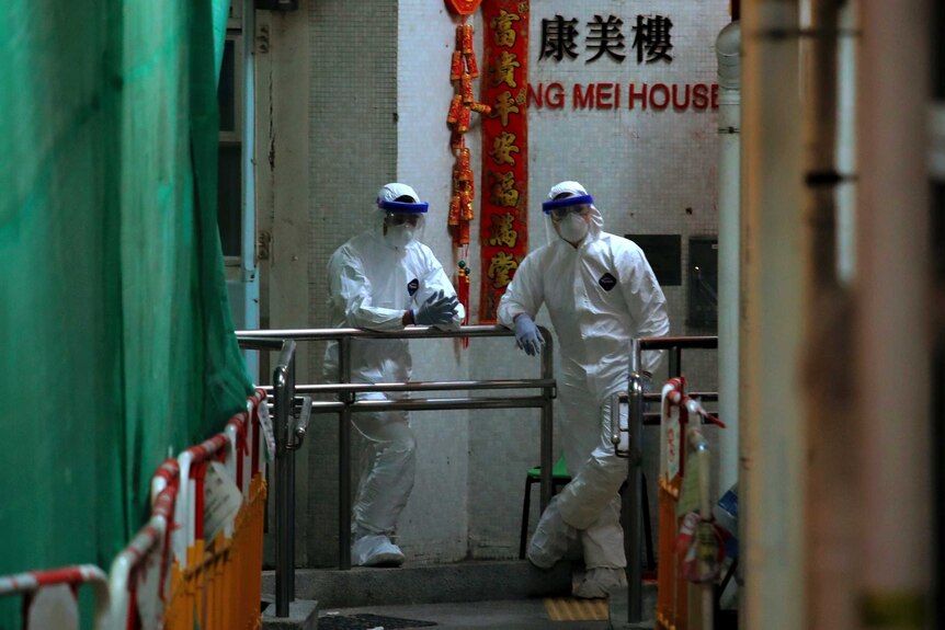Personnels wearing protective suits wait near an entrance at the Cheung Hong Estate in Hong Kong.