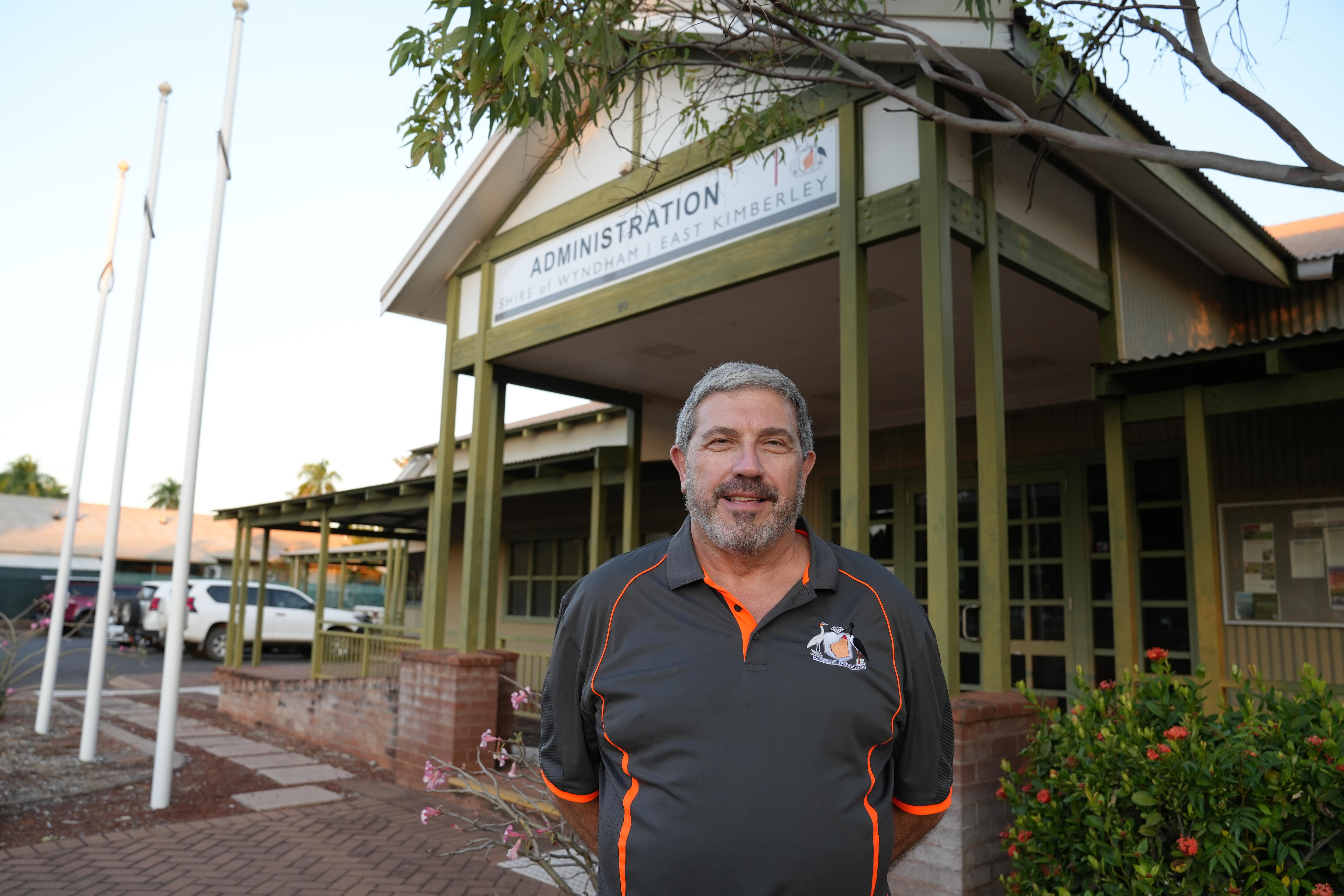 Hombre blanco de mediana edad con polo gris posando frente al edificio Shire