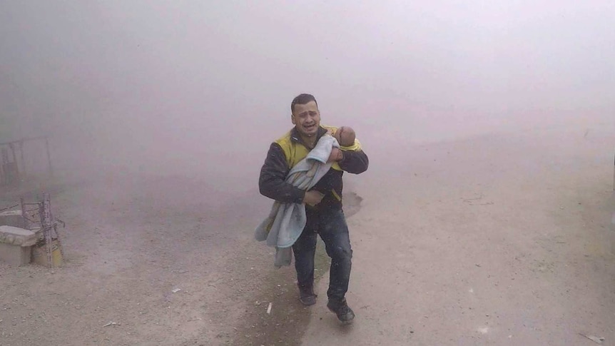 A man shrouded in dust runs along a street carrying a small boy.
