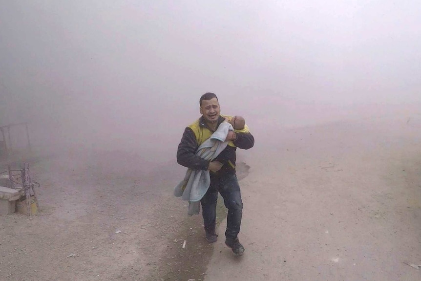 A man shrouded in dust runs along a street carrying a small boy.