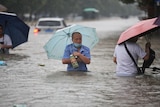 A man with an umbrella wades through waist-deep floodwater in the street.  