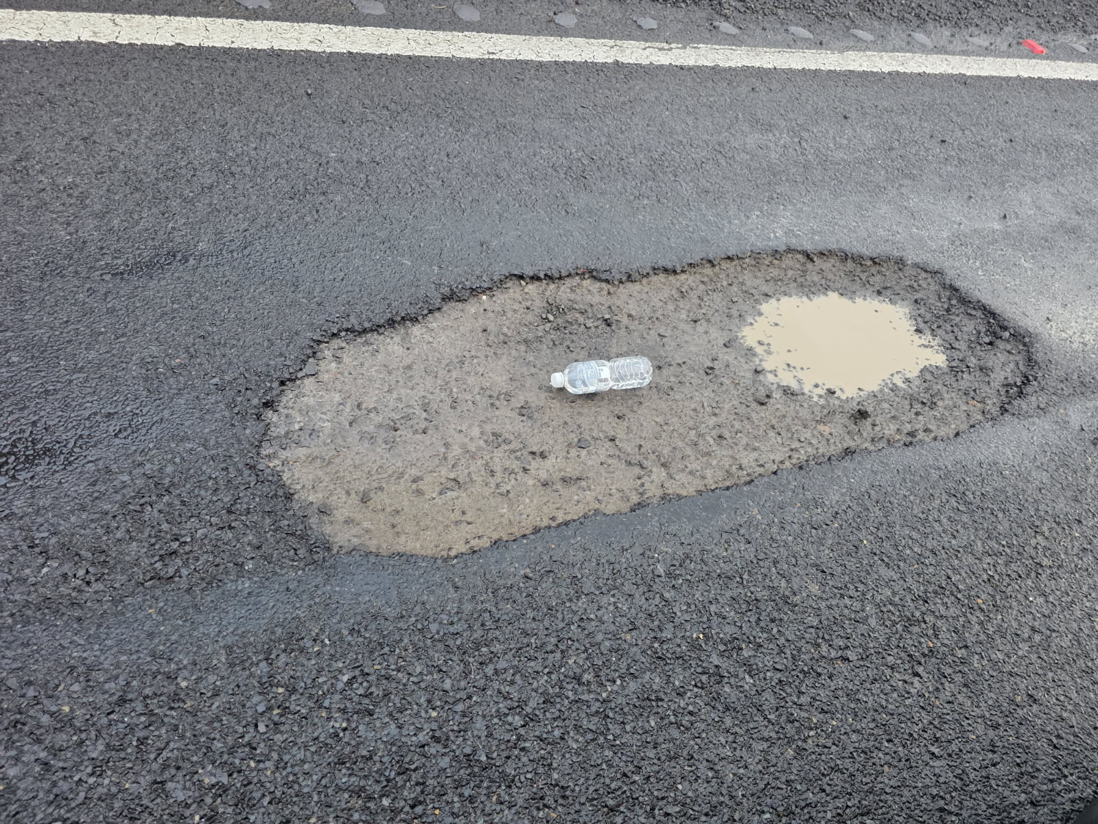 a pothole in a road with a drink bottle in it