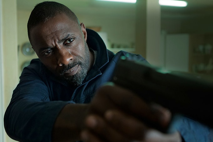 Black actor Idris Elba in the film Bastille Day. He is holding an out-of-focus pistol at arms length. Very Bond-like.