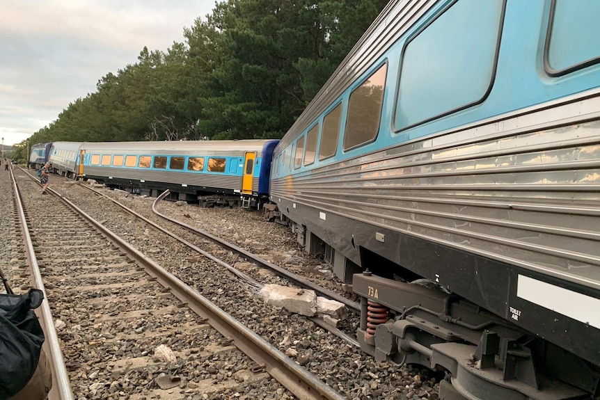 Blue-and-yellow train carriages lie off train tracks.