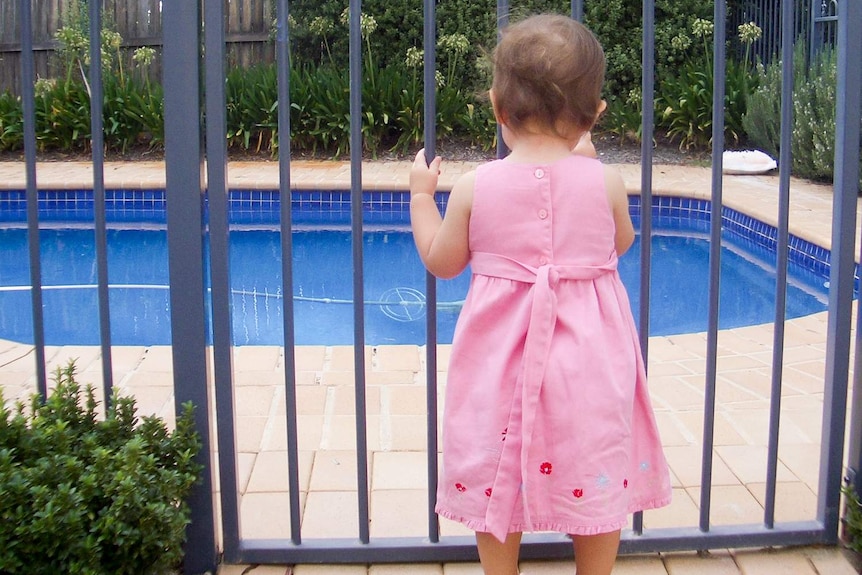 Young child standing at a backyard pool gate