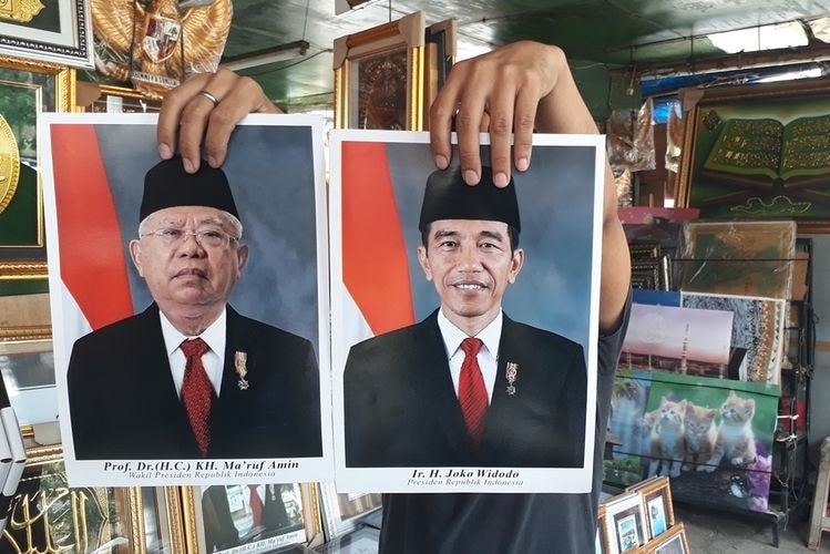 A man holds up portraits of Ma'ruf Amin and Joko Widodo.