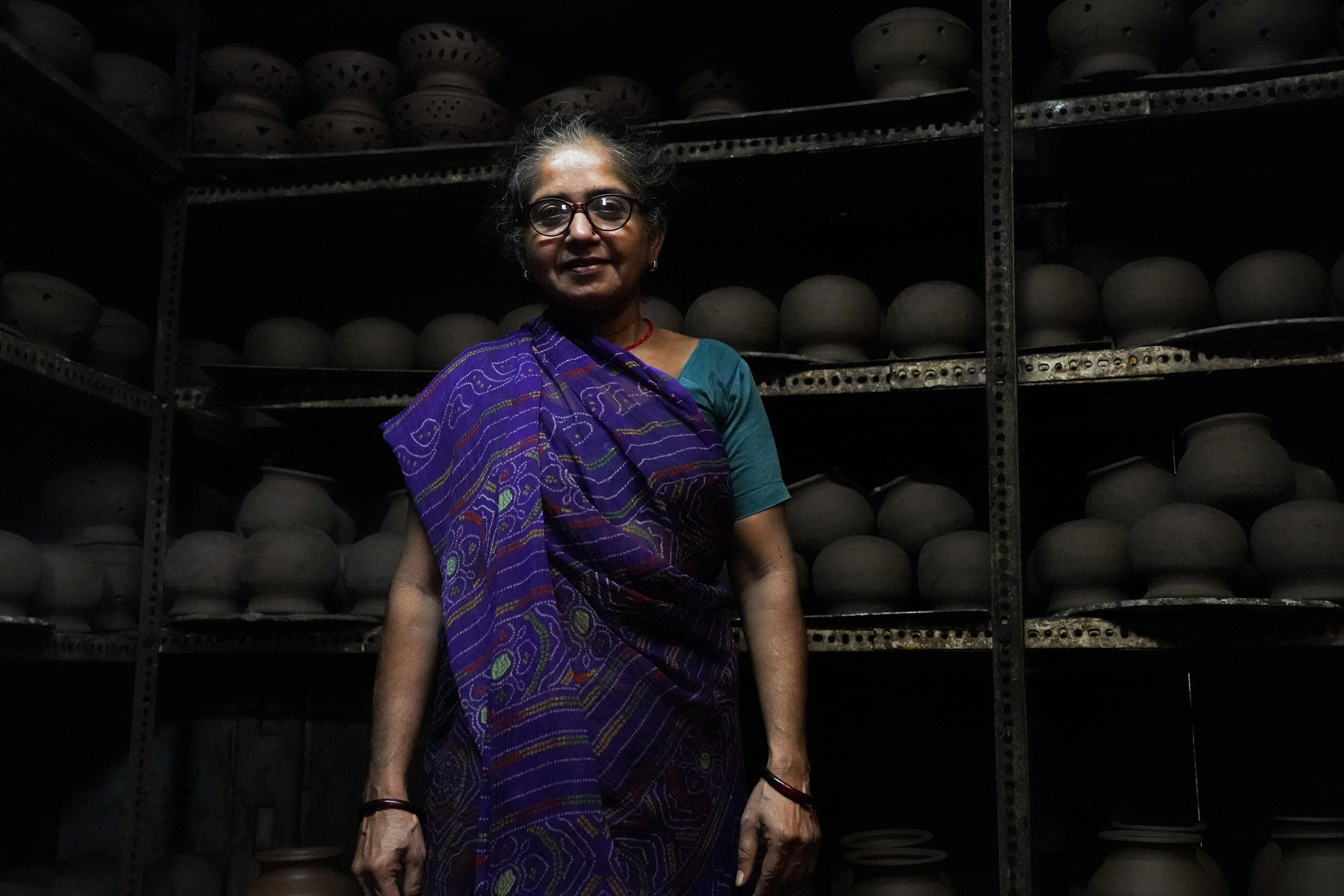A woman in a sari stands in front of shelves lined with black pots 