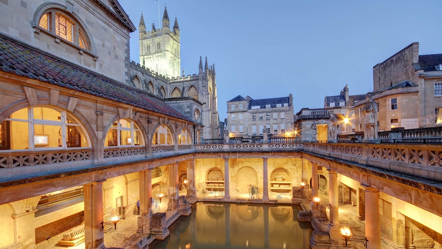 Light is reflected on the water of the old Roman baths at dusk in Bath, England.