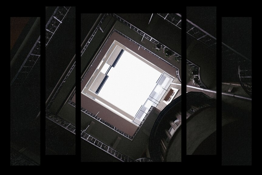 Looking up at the sky from the darkened interior of an apartment building's atrium with multiple storeys. 
