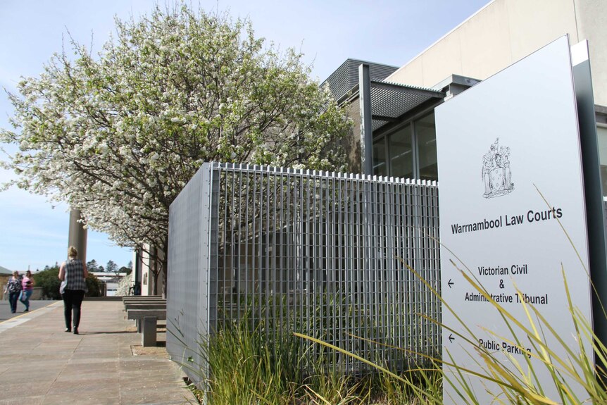 A sign that reads "Warrnambool Law Courts" in front of a large modern building and a blossoming tree.