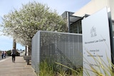 A sign reads Warrnambool Law Courts in front of a large modern building and a blossoming tree.