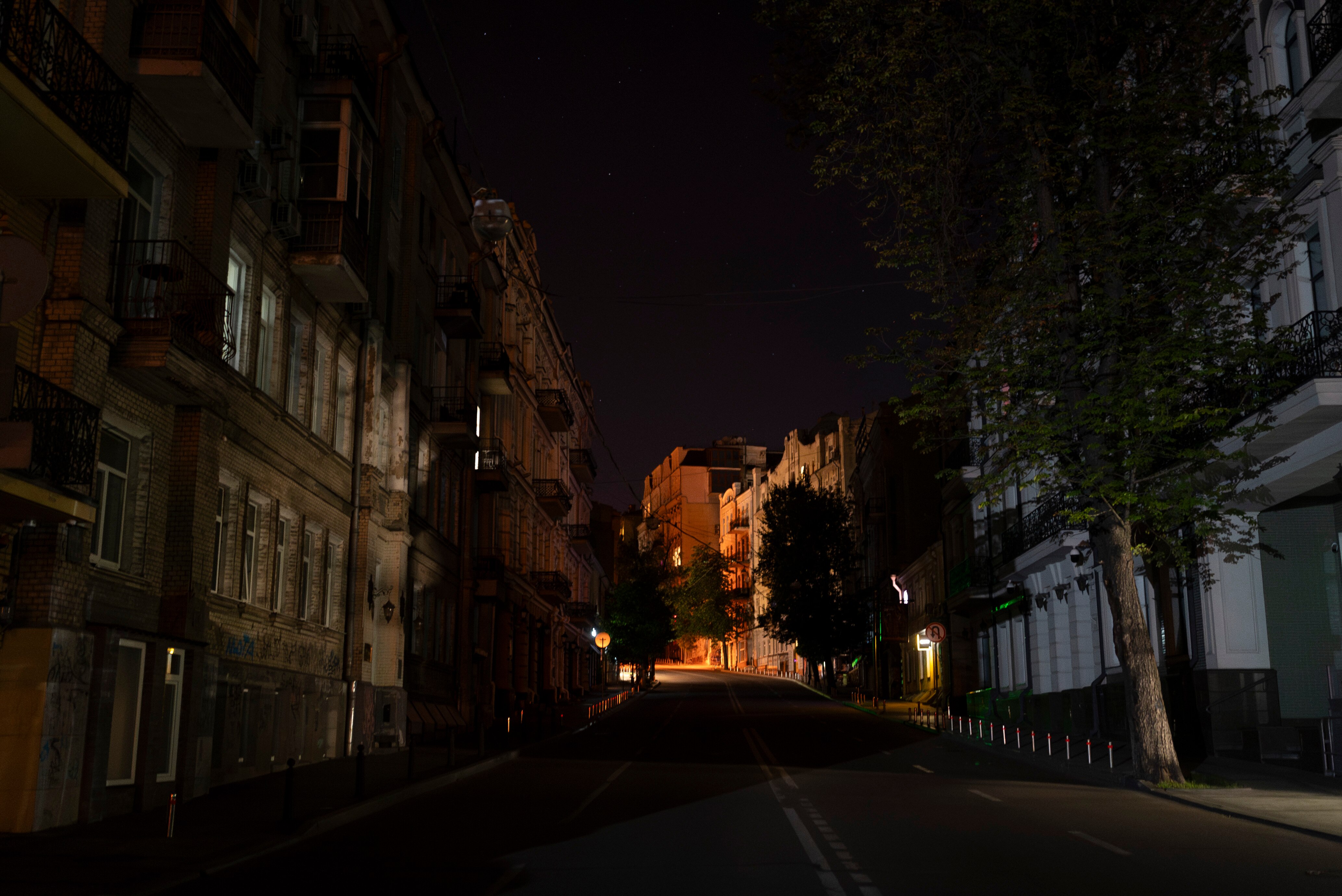 A dark tree-lined street with classical-style, multi-storey stone apartment buildings on each side
