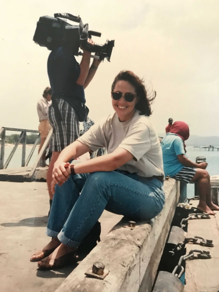 Millar sitting on jetty with cameraman filming in background.