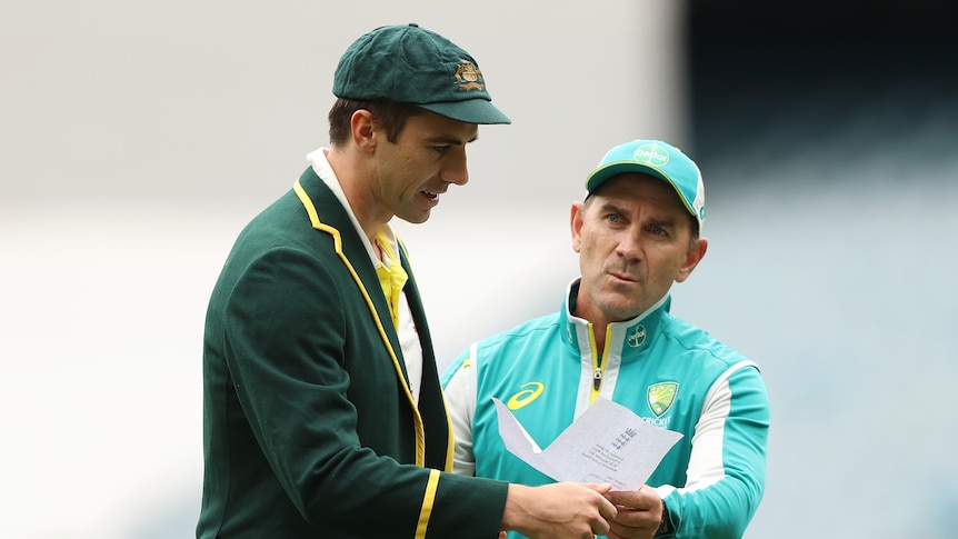A man in a green jacket and hat is handed a paper list from another man in a light green tracksuit