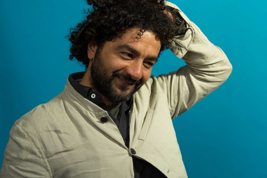 Filmmaker Mohamed Al-Daradji smiling and with one hand on curly hair.