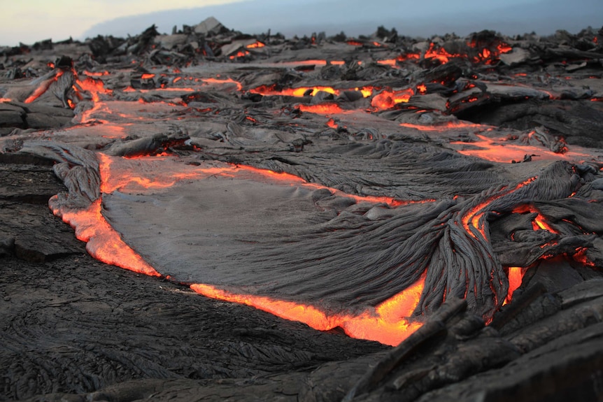Bright, burning lava surges beneath hardened, ashy rock.