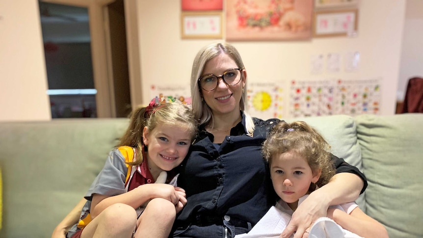 A women sits on a sofa with her arms around two girls.