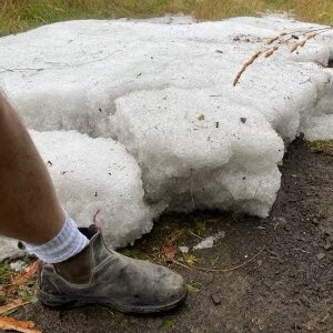A massive chunk of icy hail sits on a paddock with a leg and boot next to it for scale.