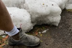 A massive chunk of icy hail sits on a paddock with a leg and boot next to it for scale.