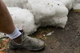 A massive chunk of icy hail sits on a paddock with a leg and boot next to it for scale.