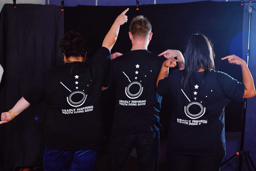 Semara Jose, Ferlin King and Tamika Young, left to right, stand in front of a black backdrop and point to their shirts.