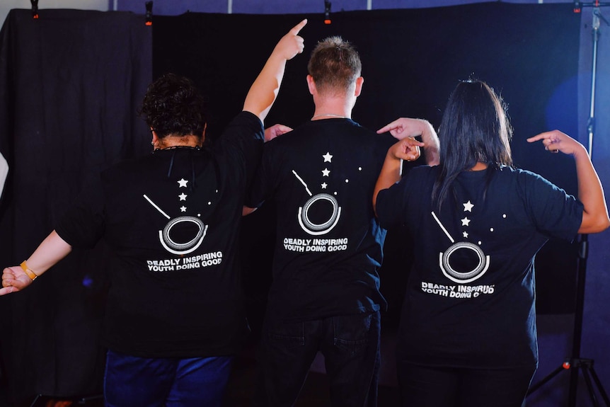 Semara Jose, Ferlin King and Tamika Young, left to right, stand in front of a black backdrop and point to their shirts.
