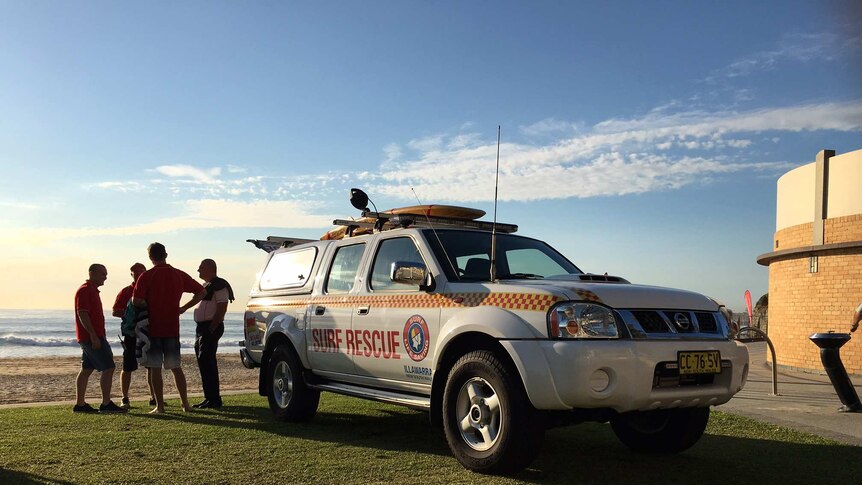 Life savers stand next to a surf rescue ute with the beach in the background.