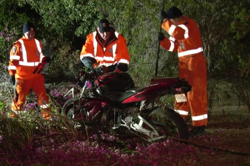 Three people in high-visibility clothing stand around a motorbike.