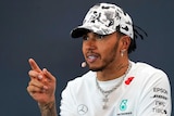 A Formula One driver gesticulates with his finger at a press conference.